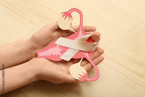 Woman with beige ribbon and paper uterus on light wooden background. Cancer a...