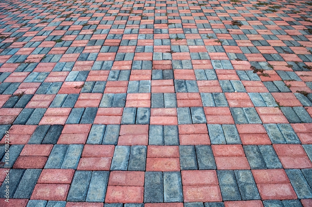 Fototapeta premium Paving stone surface featuring a pattern of red and gray bricks. The interlocking brick arrangement creates a textured ground cover suitable for walkways and driveways.