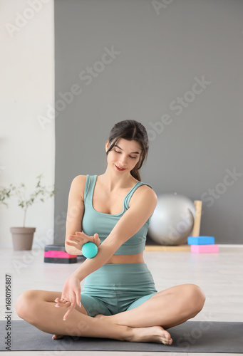 Sporty young woman massaging her arm with ball in gym