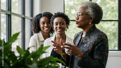An older woman speaks to two younger women in an office setting
