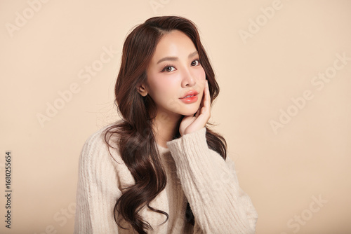 A beautiful young Asian woman with clean, fresh skin against a beige background. Skincare, facial treatment, cosmetology, beauty, and spa. An elegant portrait of an Asian woman.