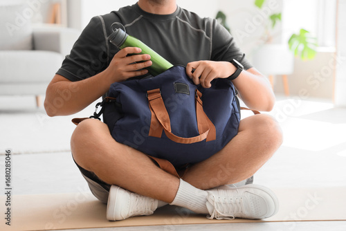 Young man preparing for gym workout, packing water bottle into sport bag, fit...
