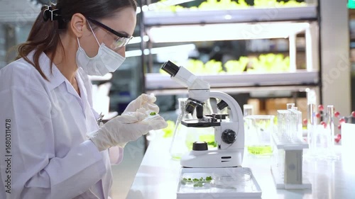 A female scientist wearing lab coat and mask conducts scientific experiments with microscope and test tubes in high tech lab.