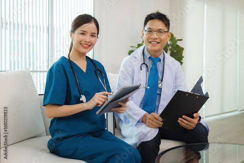Two doctors are sitting on  couch, one of them holding tablet