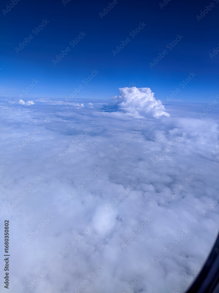 Obraz premium Expansive view above the clouds with a bright blue sky and towering cumulus formation, showcasing the beauty of aerial landscapes, peaceful atmosphere, and high-altitude travel scenery.