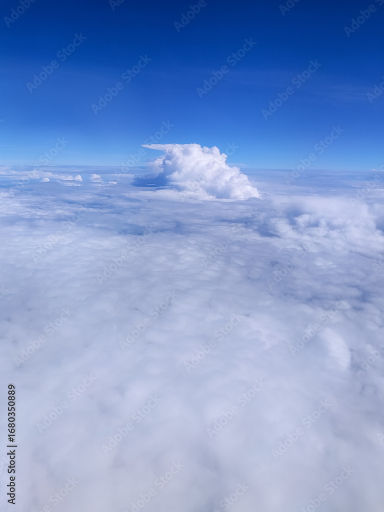 Fototapeta premium Expansive view above the clouds with a bright blue sky and towering cumulus formation, showcasing the beauty of aerial landscapes, peaceful atmosphere, and high-altitude travel scenery.