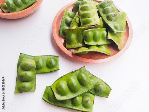 Fotografie Raw Petai (Parkia Speciosa) or Bitter Bean in a wooden plate on a white background