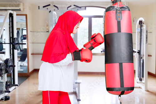 Wallpaper Mural Smiling senior Muslim woman boxing with a punching bag at the gym Torontodigital.ca