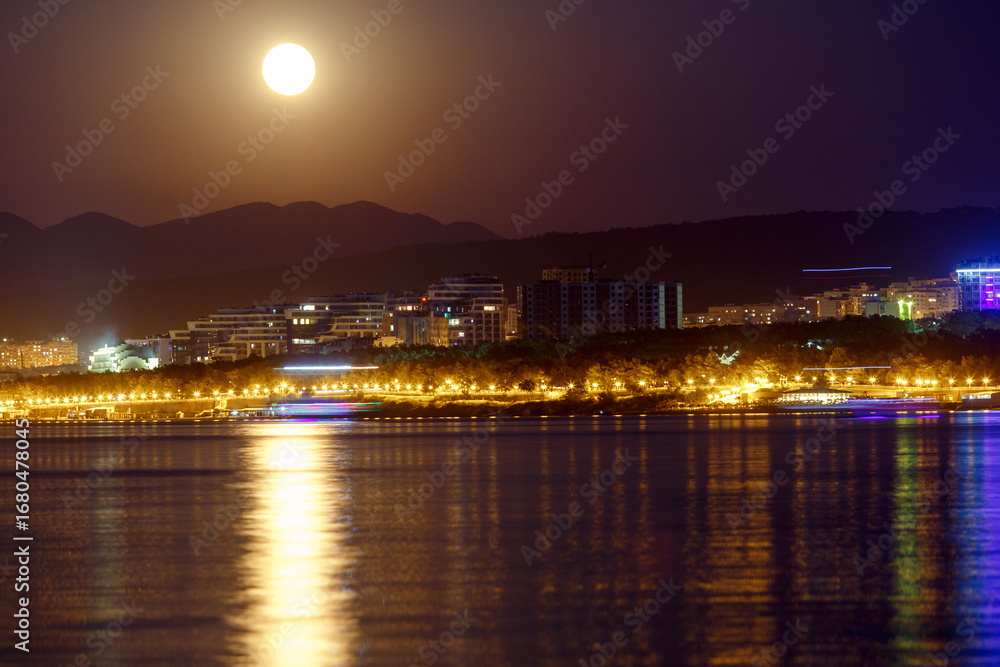 Fototapeta premium Gelendzhik resort at night by moonlight. Lights reflected in Gelendzhik Bay. Caucasus Mountains in background.