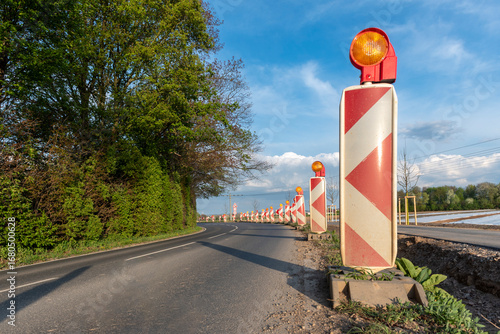 Gelbe Warnlichter auf einer Reihe von Leitbaken als Hinweis für eine Straßenbaustelle in einer unübersichtlichen Kurve in Bodenhöhe fotografiert
