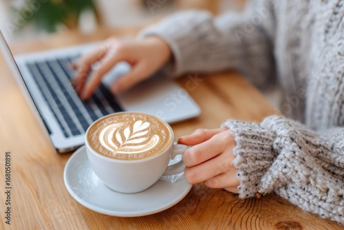 Freelancer working remotely on laptop and drinking cappuccino in cafe