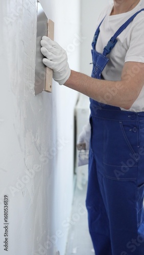 Wallpaper Mural Male construction worker wearing protective gloves and blue construction coveralls, spreading plaster smoothly across wall using professional drywall taping knife during renovation, vertical view Torontodigital.ca