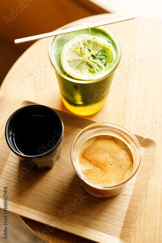 Cup of milk dirty coffee and Creation beverage of fresh matcha tea, green tea and lemon juice on wooden table by the window.