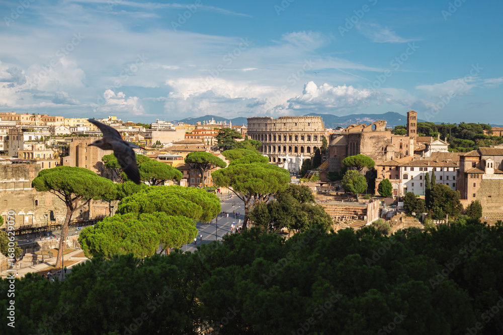 Obraz premium Panoramic View of Rome with Colosseum, Roman Ruins, and Flying Bird Over Greenery and Historic Architecture