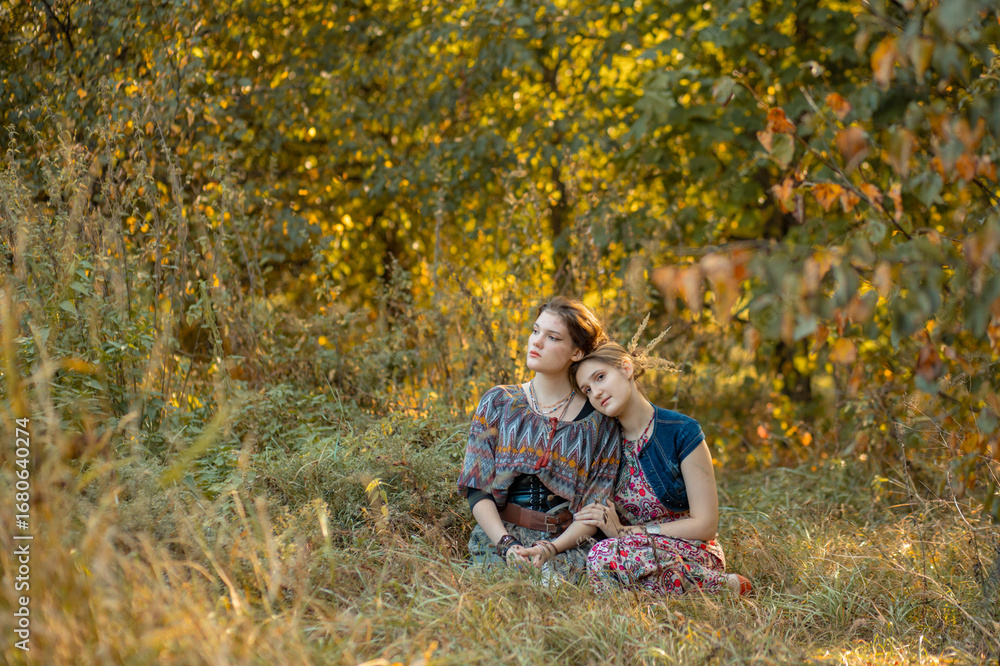 Fototapeta premium Two young women are looking forward to the sunset. Best friends, sisters. Two girls are relaxing in a forest clearing.