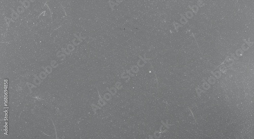A macro photograph of a flat, solid gray surface showing subtle texture, faint scratches, and dust particles.