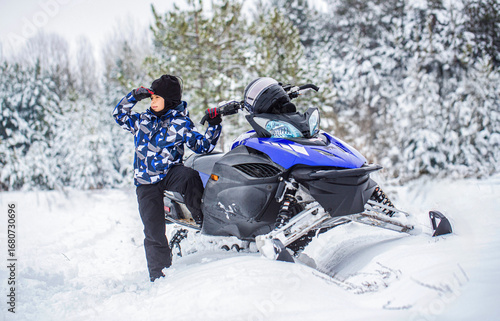 Foto Child rides a blue snowmobile on a snowy trail, forest