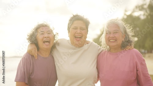 Happy Asian senior woman friends walking together on the beach at sunset. Group of Healthy wellness elderly people enjoy and fun outdoor lifestyle travel nature the sea on summer holiday vacation.