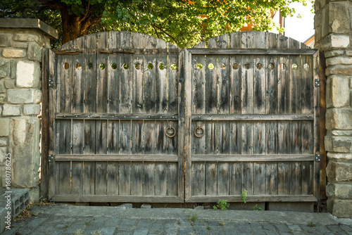Fotografie Large old wooden double gates with iron rings and circular cut-outs, framed by stone pillars in Mtskheta, Georgia