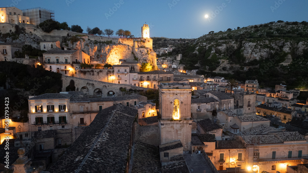 Fototapeta premium Modica by night – winding streets glowing with golden lights, baroque houses climbing the hillsides, and a timeless Sicilian charm captured from above.