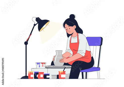 Young woman artist creating pottery on a wheel under a desk lamp with art supplies around her workspace
