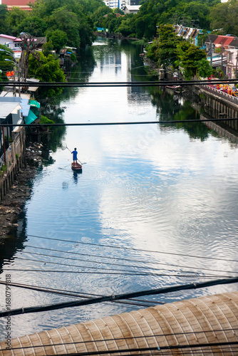 ​A high-angle view captures the solitude of a person on a boat, creating a peaceful moment that reflects the sky in the heart of an urban waterway