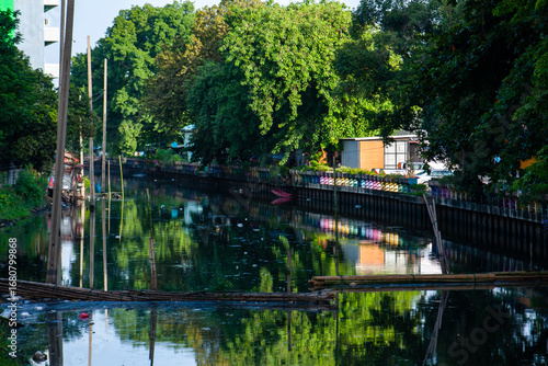 ​The image captures the duality of an urban waterway: a tranquil, reflective surface that coexists with the signs of human life and urban decay