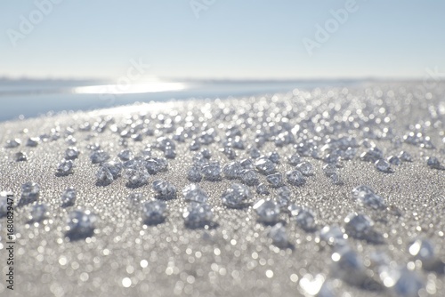 Many small, reflective gems on light beige sand near water