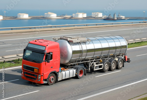 Road Fuel Tanker With Stainless Hull Tank With Oil Gas Marine Terminal In The Background