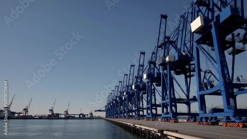 Industrial Loading Cranes Operating on Pier in Dockyard Against Blue Sky