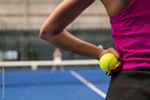 Diverse female opponents holding tennis ball readying serve over net on court, copy space