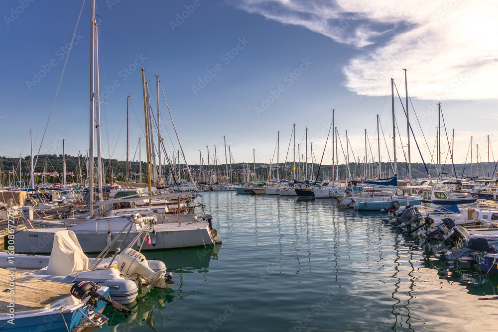 Fototapeta premium scenic marina with sailboats and yachts under clear blue sky at golden hour. colorful seascape with small marina in warm