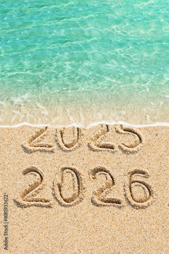 New Year concept - 2025 and 2026 written on the beach, blue ocean wave and sand