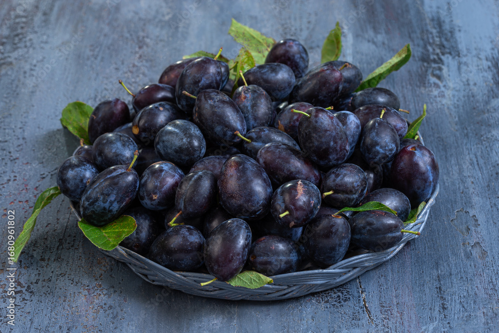 Fototapeta premium Freshly harvested dark plums in woven basket