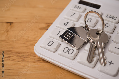 House key on calculator with wooden table background copy space. Homebuyers, mortgage loan, banking, real estate investment trust (REIT), reverse mortgage, home selling or rental and so on concept.