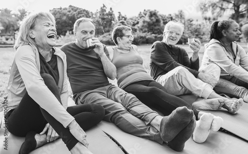 Senior people having fun drinking hot tea after yoga lesson at city park - Joyful elderly lifestyle and sport concept - Focus on left latin woman face - Black and white editing