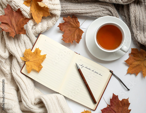 Flat lay of autumn journal with handwritten notes, cup of tea, dried leaves, cozy blanket, natural light, creative workspace photography