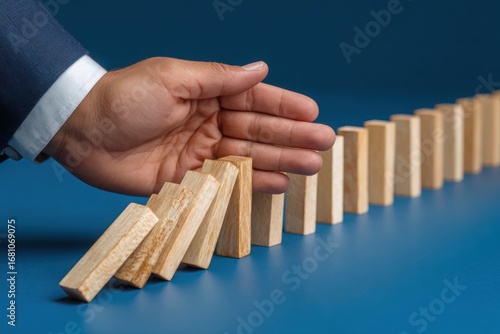 Businessman s hand stopping a line of falling dominoes to prevent a cascade effect
