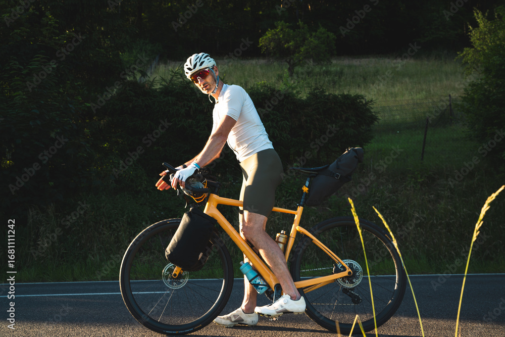 Obraz premium Radfahrer fährt auf gelben Fahrrad und Gepäck auf der Strasse in den Sonnenuntergang, bikpacking, Radreise