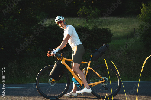 Radfahrer fährt auf gelben Fahrrad und Gepäck auf der Strasse in den Sonnenuntergang, bikpacking, Radreise
