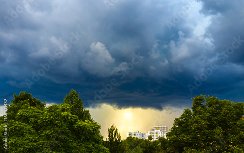 Ominous thunderclouds over landscape with trees and city buildings