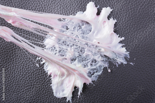 Chewing gum has become stuck to a dark textured surface, showing its stretching and gooey consistency. The leather surface shows intricate texture as the cleaning care. Daily stains concept