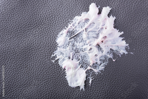 Chewing gum has become stuck to a dark textured surface, showing its stretching and gooey consistency. The leather surface shows intricate texture as the cleaning care. Daily stains concept