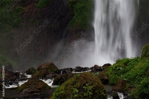 Pelangi Waterfall, West Bandung, Indonesia, surrounded by lush green foliage, vibrant nature, rainbow mist, cascading water, serene, tropical scenery, eco-tourism, hiking.