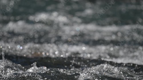Close-up view of a small river with rushing churning water reflecting the sun creating highlights
