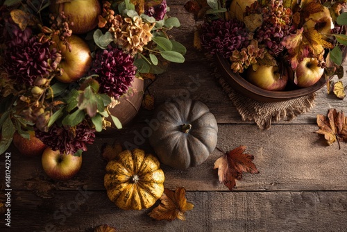 A rustic autumnal display of pumpkins, apples, flowers, and leaves on a weathered wooden surface, evoking a sense of harvest and tranquility.