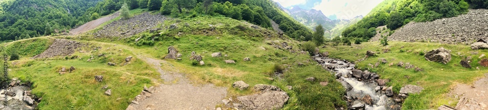 Naklejka premium Panoramic view of a lush green valley with a stream and rocks