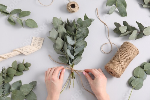 Foto Florist making beautiful bouquet of eucalyptus branches at white table, top view