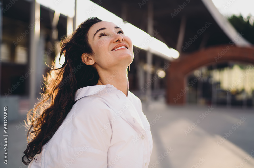 © BullRun - Smiling woman in white shirt looking upward with optimistic expression outdoors. Conceptual portrait of freelancer lifestyle symbolizing empowerment, positivity, and digital future.