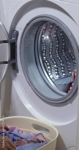 woman with basket doing laundry at home, female hand loading colour laundry into the drum of washing machine.